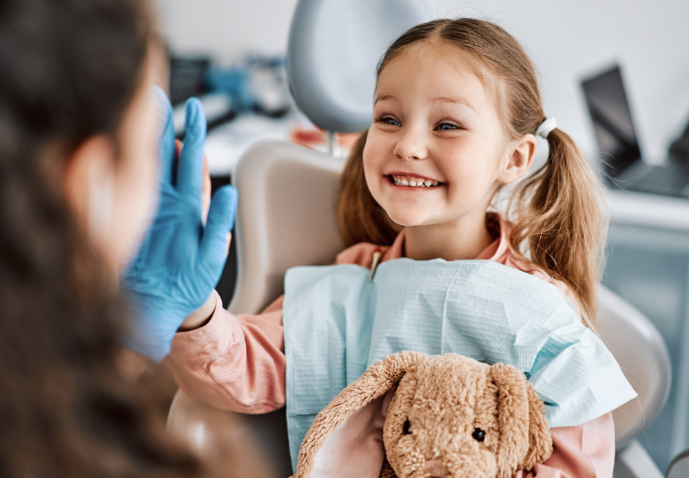 a child sitting in a dental chair while holding a teddy bear